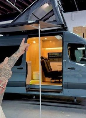 Homme pointant un van aménagé avec un espace de vie et un toit relevable.